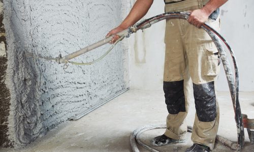 Worker plastering the interior wall with an automatic spraying plaster pump machine